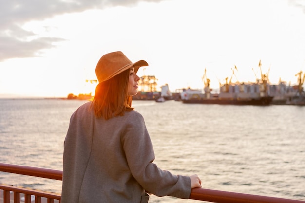 Mujer elegante con sombrero de fieltro y abrigo al amanecer en el mar