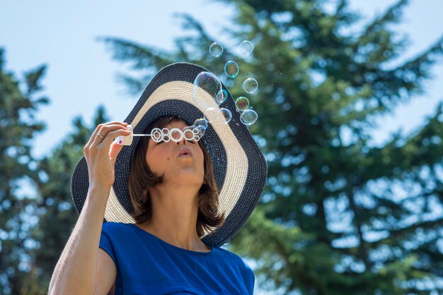 Mujer elegante en un sombrero de paja que sopla burbujas