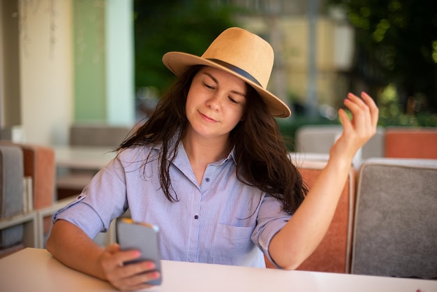 Mujer elegante con sombrero con teléfono inteligente afuera