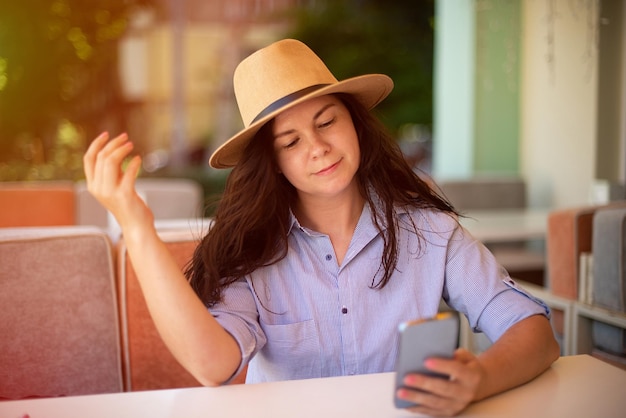 Mujer elegante con sombrero con teléfono inteligente fuera del sol en el fondo