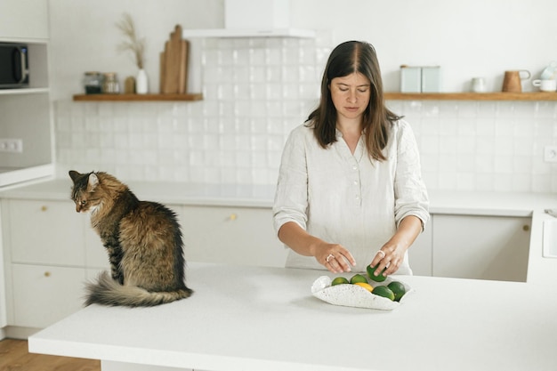 Mujer elegante y su gato en una nueva cocina blanca mínima Ama de casa limpiando la cocina después de mudarse con una linda mascota en un nuevo hogar moderno