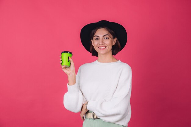 Mujer elegante en suéter blanco casual y sombrero en la pared roja rosa