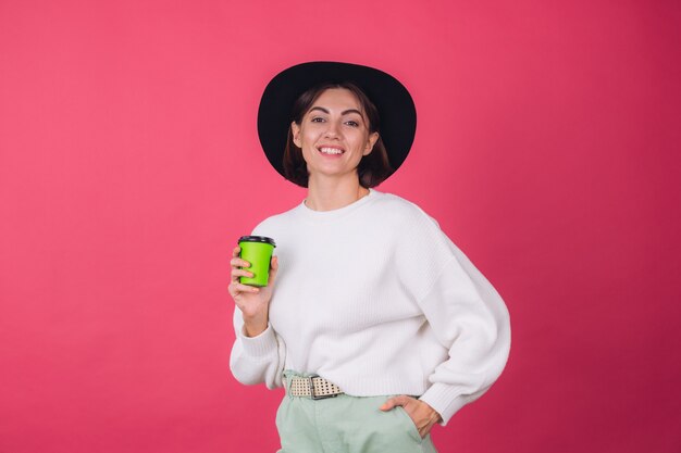 Mujer elegante en suéter blanco casual y sombrero en la pared roja rosa