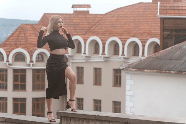 Mujer elegante en traje negro y tacones Modelo sexy joven posa para la foto sobre fondo de arquitectura antigua