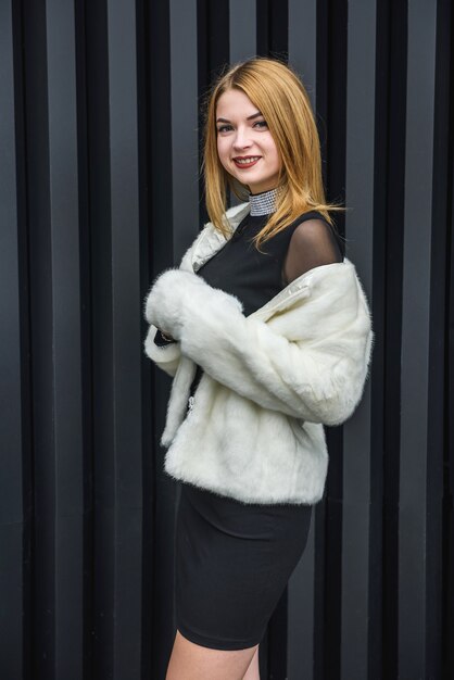 Mujer elegante en vestidito negro y con pañuelo de piel posando afuera. Concepto de moda