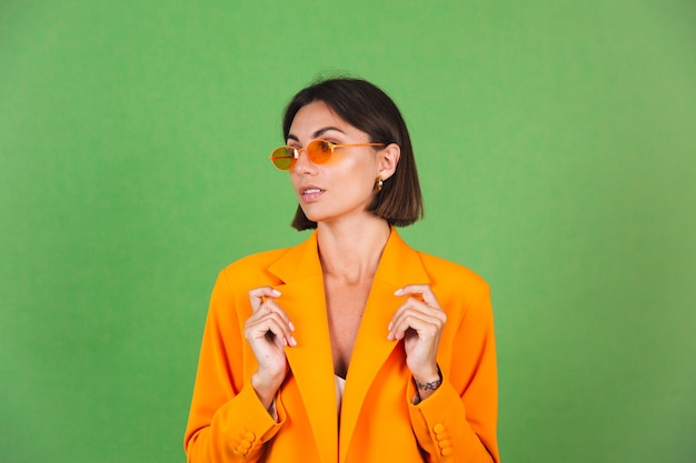 Mujer elegante en vestido beige de seda y blazer naranja de gran tamaño en verde, sonrisa de emociones positivas