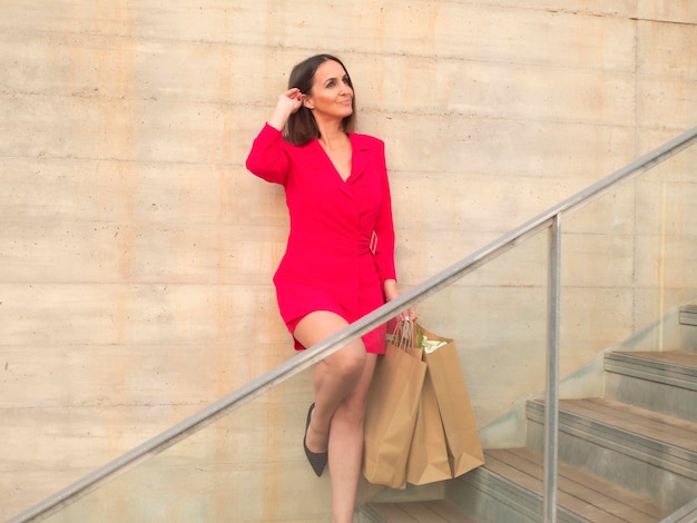 Foto mujer elegante con vestido rojo parada en las escaleras con bolsas de compras