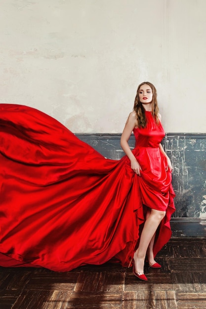 Mujer elegante en vestido rojo que sopla. Hermosa modelo de moda sobre fondo azul