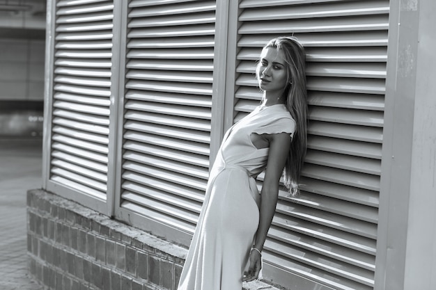 Mujer elegante viste vestido de moda posando en la calle cerca de persianas metálicas. Copie el espacio. Color monocromático