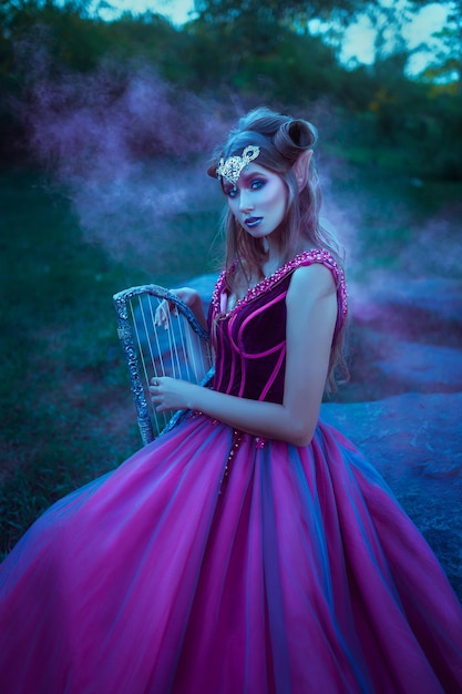 Foto mujer elfa en vestido morado con arpa en manos