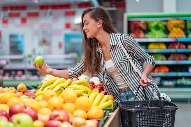 La mujer elige fruta fresca en supermercado. cliente que compra comida en la tienda de comestibles