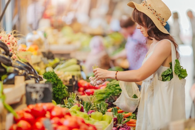 La mujer elige frutas y verduras en el mercado de alimentos. Bolsa ecológica reutilizable para compras. Concepto de desperdicio cero.