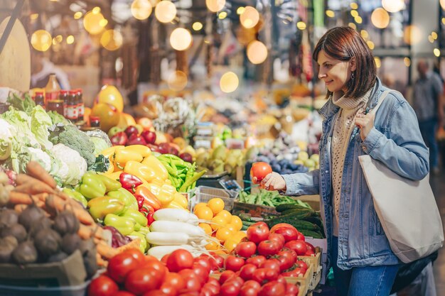 La mujer elige frutas y verduras en el mercado de alimentos. Bolsa ecológica reutilizable para compras. Estilo de vida sostenible. Concepto ecológico.