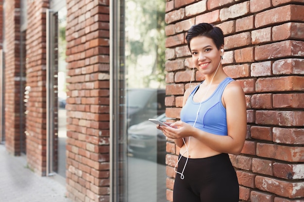 Mujer elige música para escuchar en su teléfono móvil mientras trota en la ciudad, copia espacio