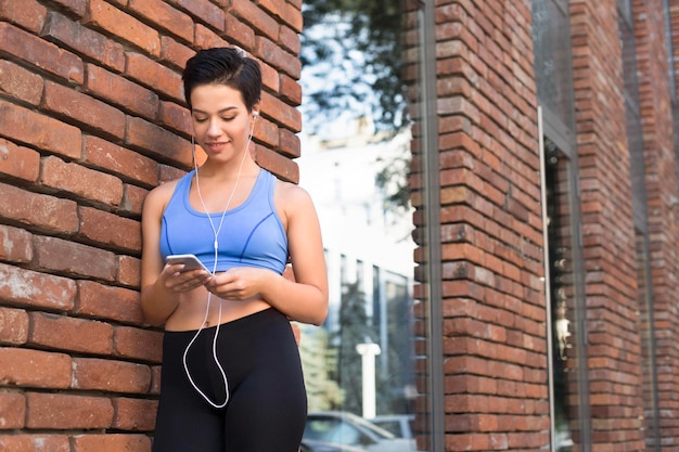 Mujer elige música para escuchar en su teléfono móvil mientras trota en la ciudad, copia espacio