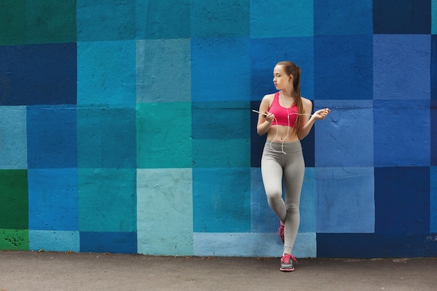 La mujer elige música para escuchar en el teléfono inteligente durante el jogging en la ciudad, copie el espacio, fondo colorido