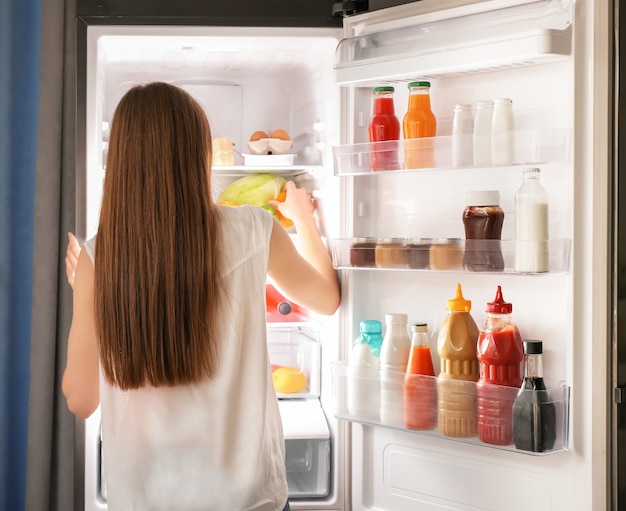 Mujer eligiendo alimentos en el frigorífico en casa