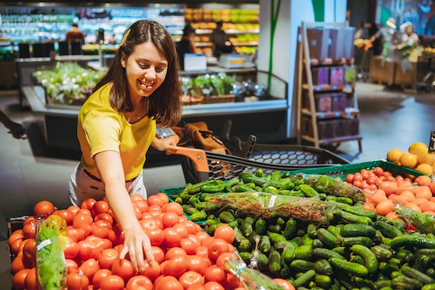 Mujer eligiendo tomates rojos de la tienda de comestibles