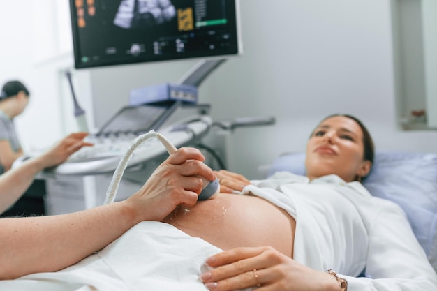 Foto una mujer embarazada está acostada en el hospital y el médico le hace una ecografía.