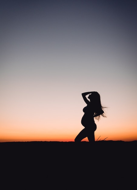 Foto mujer embarazada adulta joven se encuentra en el campo al atardecer concepto de maternidad y fertilidad