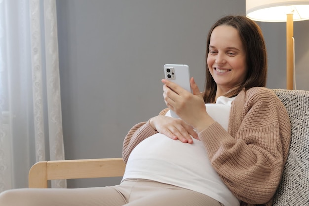 Mujer embarazada alegre disfrutando de la comunicación en línea en un foro para mujeres embarazadas navegando por páginas web de Internet leyendo información sobre el cuidado de los bebés