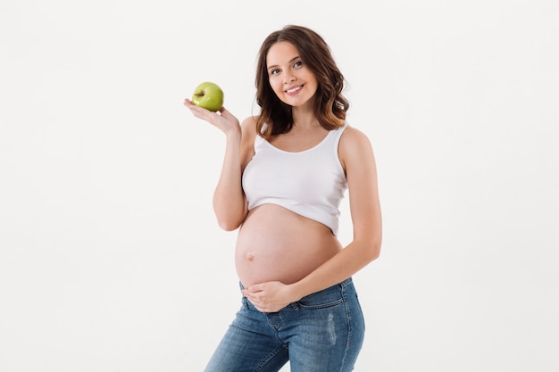 Mujer embarazada alegre que come la manzana