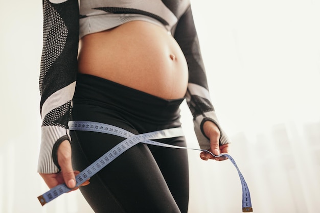 Mujer embarazada anónima haciendo mediciones con cinta adhesiva después del entrenamiento