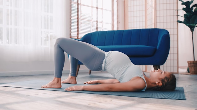 Mujer embarazada asiática haciendo ejercicios de yoga en casa.