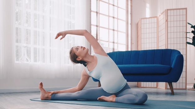 Mujer embarazada asiática haciendo ejercicios de yoga en casa.