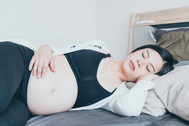 Mujer embarazada asiática hermosa joven que duerme en cama