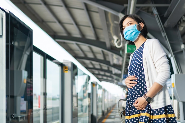 Foto mujer embarazada asiática en mascarilla esperando tren de cercanías para viajar