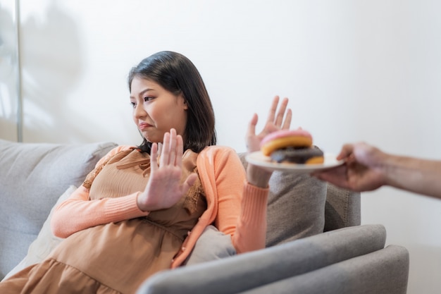 La mujer embarazada asiática rechaza la comida chatarra o la comida poco saludable como las donas por su salud y la del bebé. Dieta y buena salud para el concepto de madre.