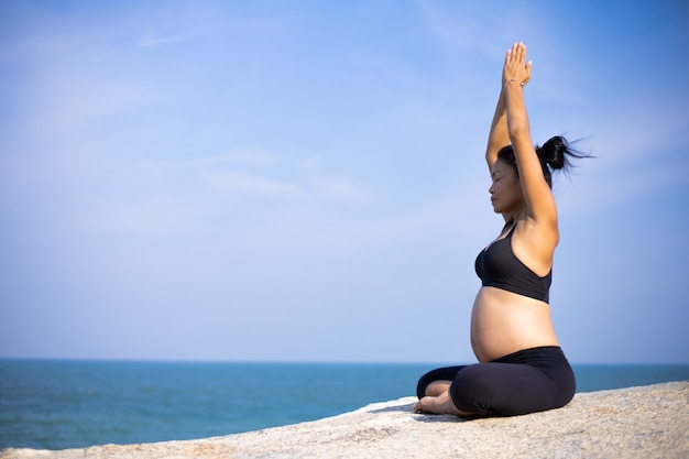 Mujer embarazada asiática yoga en la playa atardecer verano