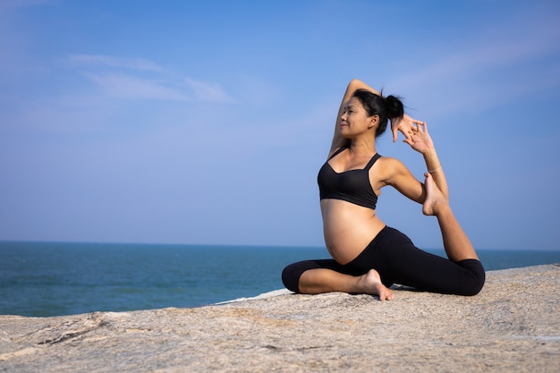 Mujer embarazada asiática yoga en la playa atardecer verano