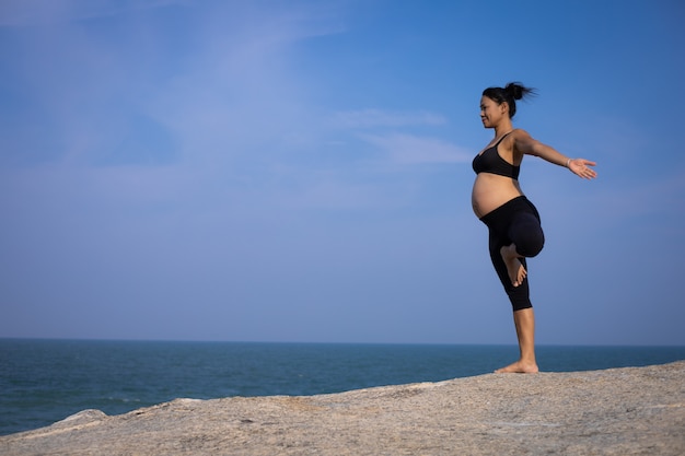 Mujer embarazada asiática yoga en la playa atardecer verano