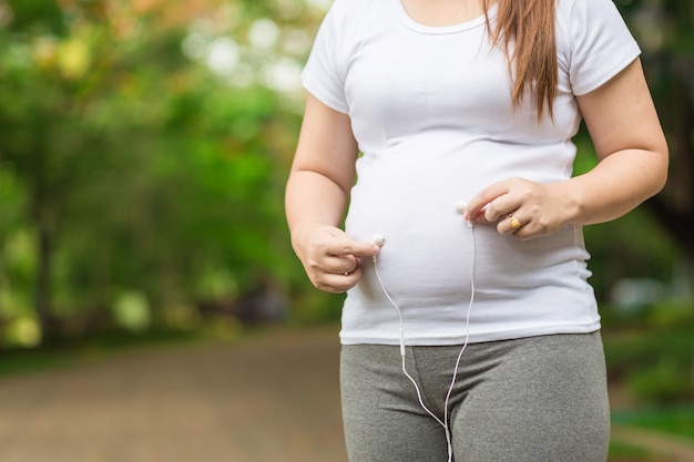 Mujer embarazada con auriculares en su vientre en el jardín