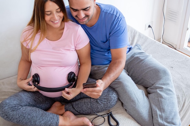 mujer embarazada con auriculares en el vientre y marido tocando música con el teléfono para el bebé