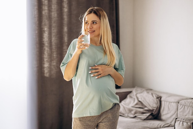 Mujer embarazada bebiendo agua en casa