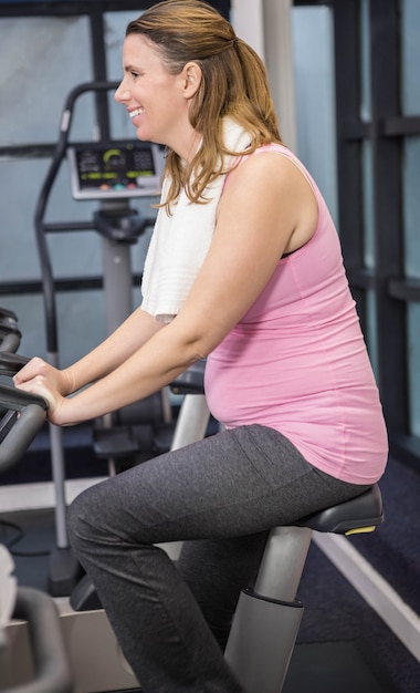 Mujer embarazada en bicicleta de ejercicio en el gimnasio