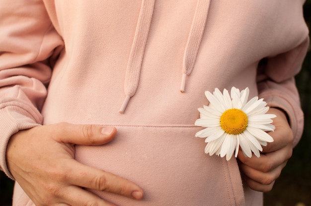 Una mujer embarazada con una blusa rosa sostiene su estómago y un primer plano de margarita con la mano