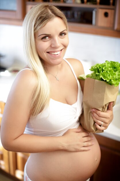 Mujer embarazada con bolsa de papel con ensalada de hojas