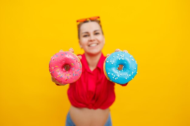 Una mujer embarazada brillante con una camisa rosa sobre un fondo amarillo come rosquillas dulces rosquillas dulces frescas en las manos de una mujer embarazada