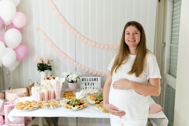 Foto mujer embarazada en el buffet de la ducha de bebé con varios aperitivos y postre dulce esperando unas vacaciones infantiles en la familia