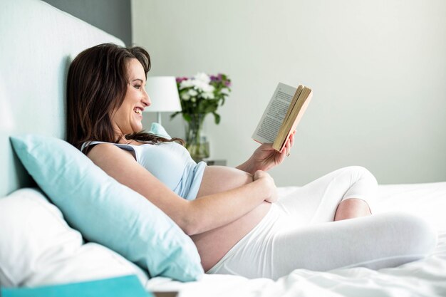 Mujer embarazada en la cama leyendo un libro en casa