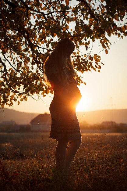 Mujer embarazada caminando al aire libre en la puesta de sol