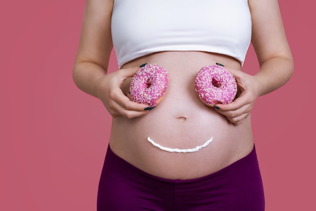 Mujer embarazada con cara divertida en su estómago y ojos de rosquilla.