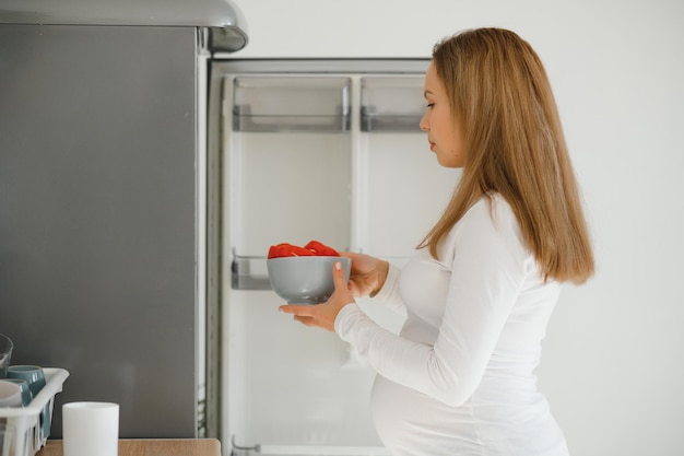 Foto mujer embarazada en casa en la cocina abre el refrigerador