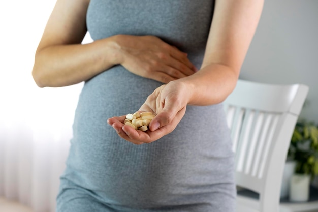 Mujer embarazada en casa con pastillas en las manos Expectativa del bebé Atención médica y vitaminas prenatales durante el embarazo Enfermedad y medicina durante el embarazo