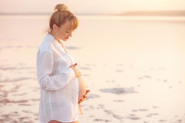 Mujer embarazada caucásica adulta contra el telón de fondo de la puesta de sol Niña embarazada relajarse afuera