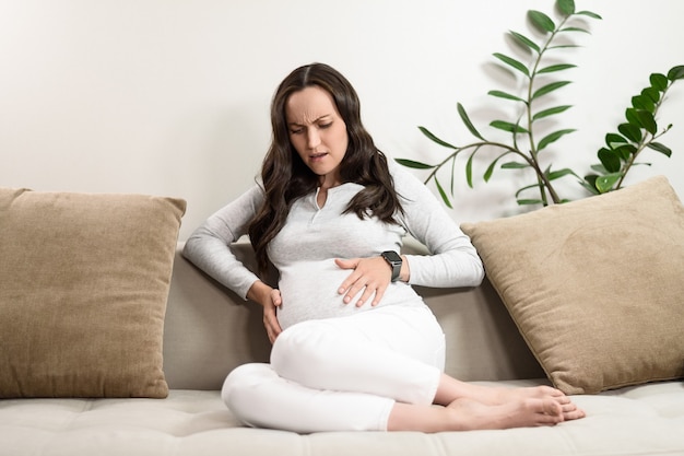 Mujer embarazada caucásica experimenta dolor, malestar abdominal, dolores de parto, dolores de parto